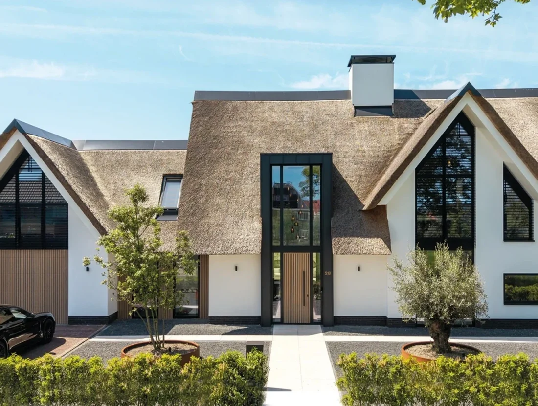 Moderne villa met rieten kap, witte gevel, houten accenten en grote raampartijen, ontworpen door Bekhuis & KleinJan.