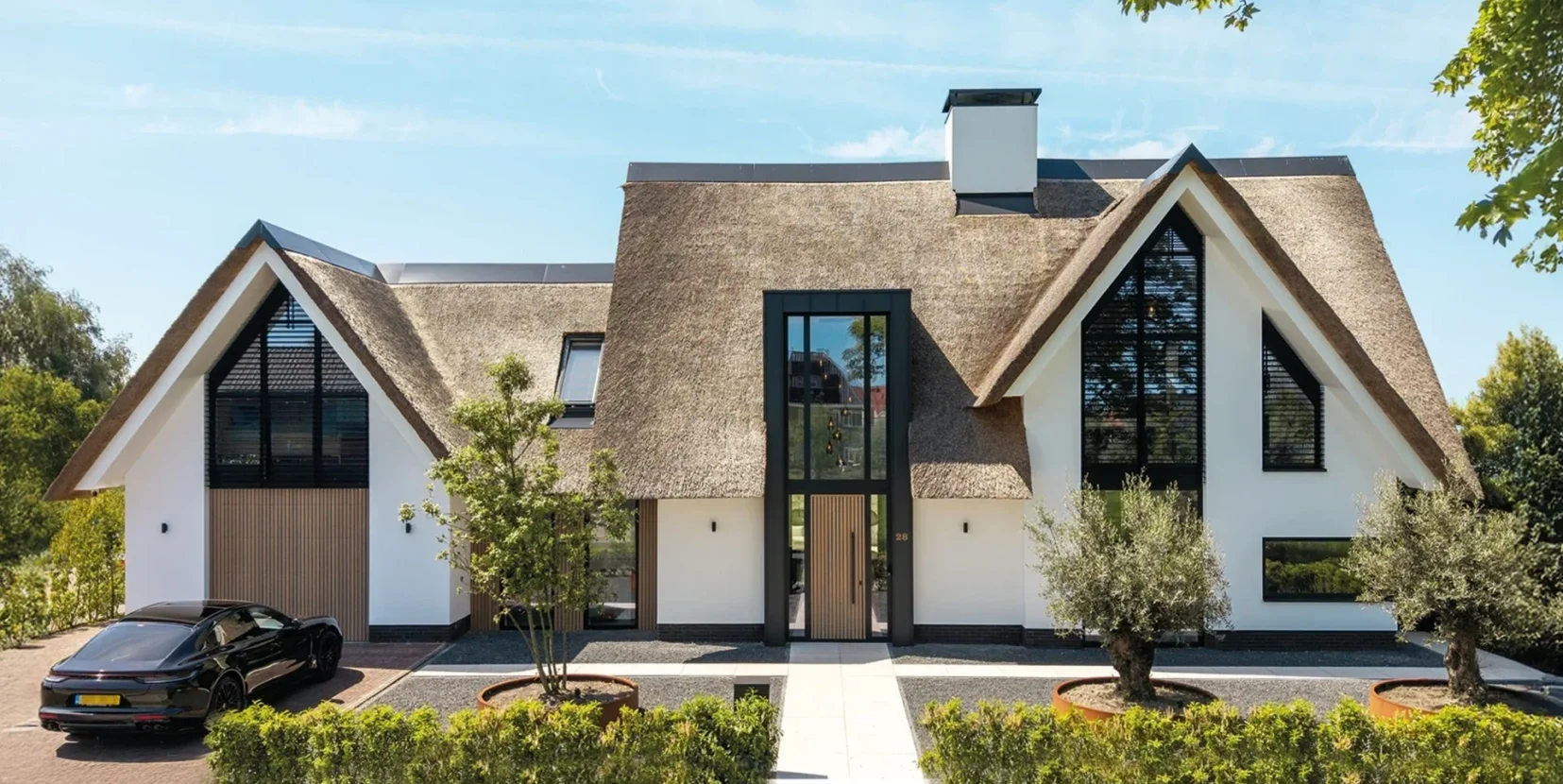 Moderne villa met rieten kap, witte gevel, houten accenten en grote raampartijen, ontworpen door Bekhuis & KleinJan.