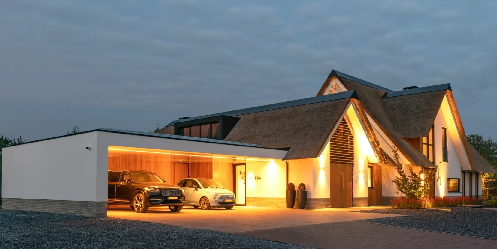 Landelijk-moderne villa in met verlichte gevels, rieten dak en en een overdekte carport