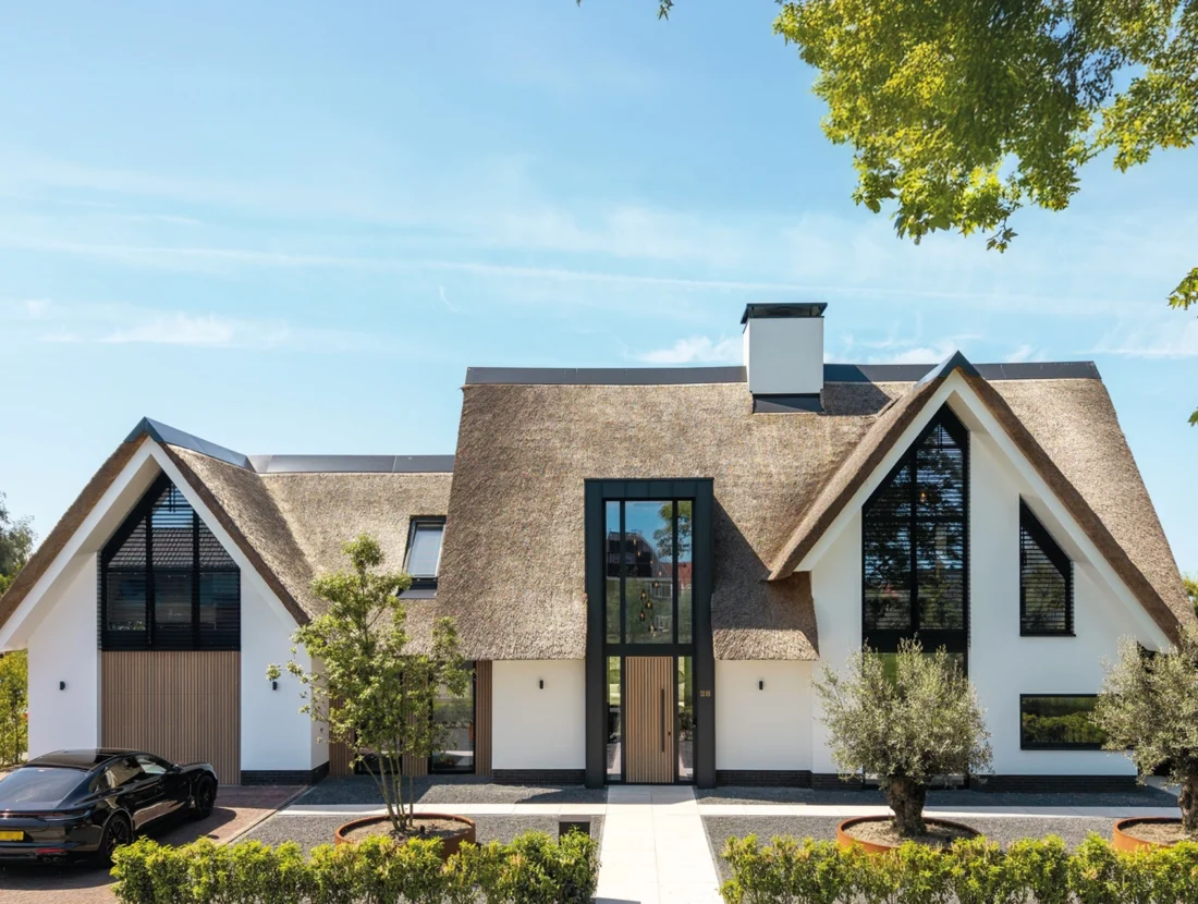 Moderne villa met rieten kap, witte gevel, houten accenten en grote raampartijen, ontworpen door Bekhuis & KleinJan.