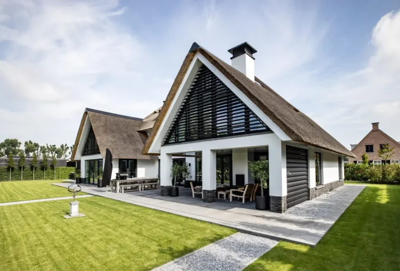 Klassieke villa met rieten dak, zwarte lamellen in de topgevels en een overdekt terras aan de achterzijde.
