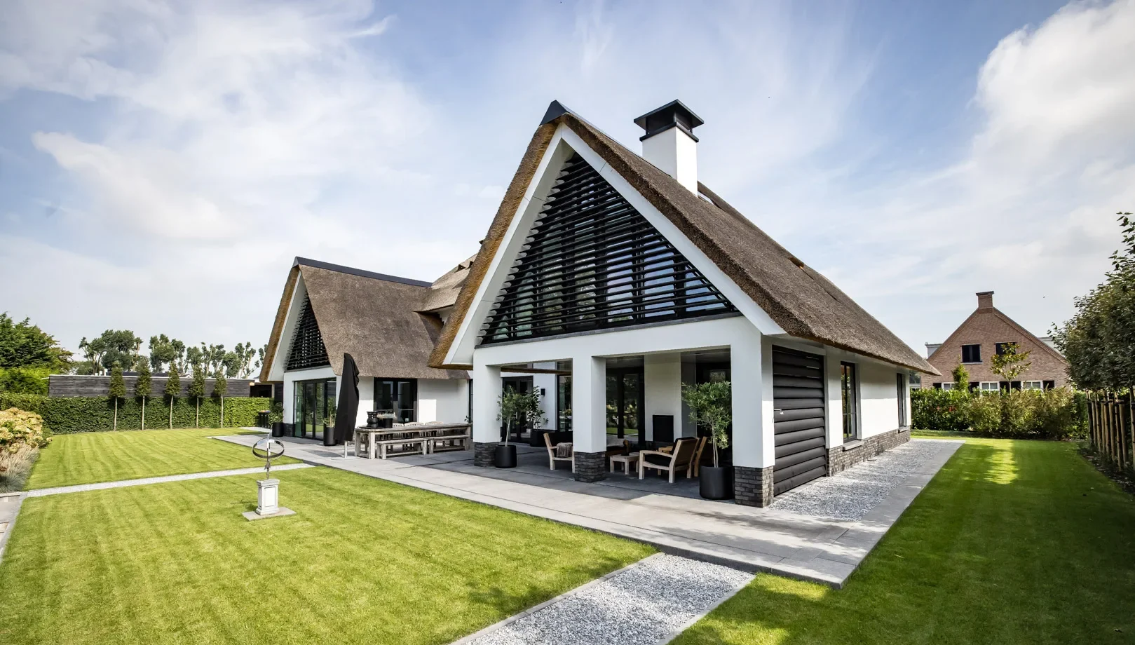 Klassieke villa met rieten dak, zwarte lamellen in de topgevels en een overdekt terras aan de achterzijde.