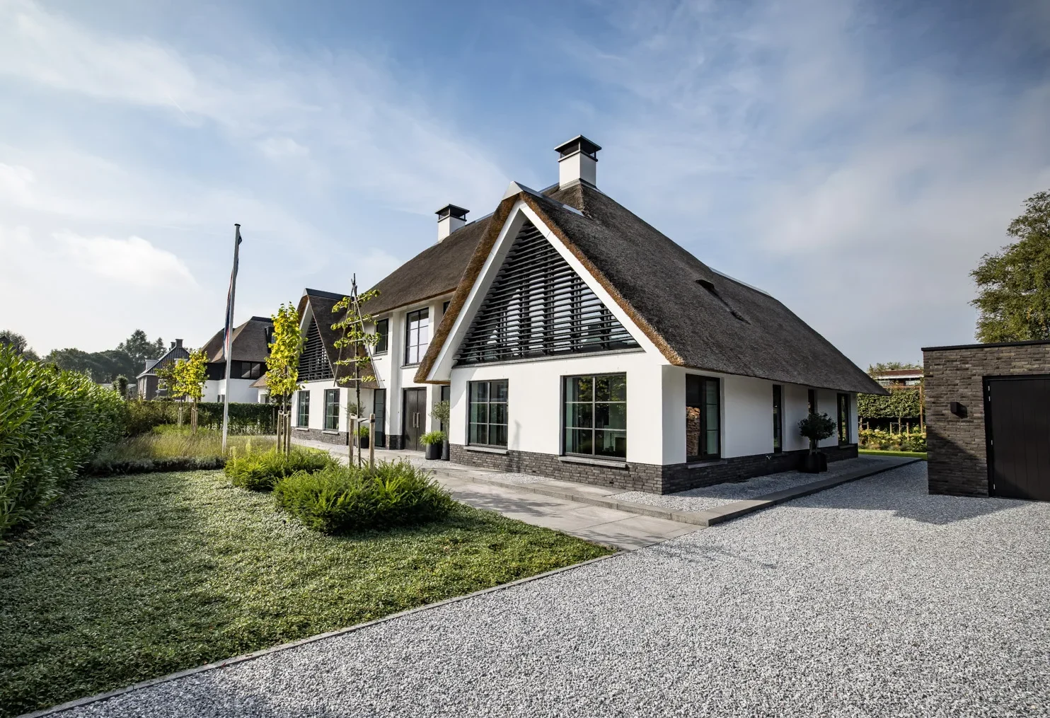 Voorzijde van een klassieke witte villa met rieten dak, zwarte kozijnen en een ruime grindoprit, ontworpen door Bekhuis & KleinJan