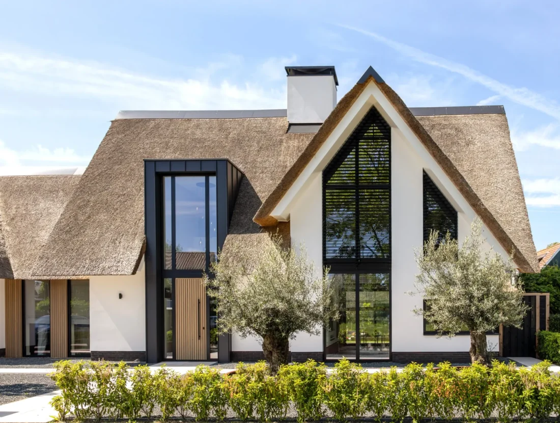 Moderne villa met rieten kap, witte gevel, houten accenten en grote raampartijen, ontworpen door Bekhuis & KleinJan.