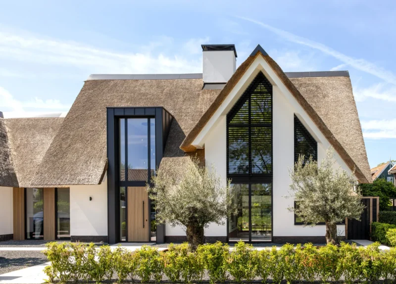 Moderne villa met rieten kap, witte gevel, houten accenten en grote raampartijen, ontworpen door Bekhuis & KleinJan.