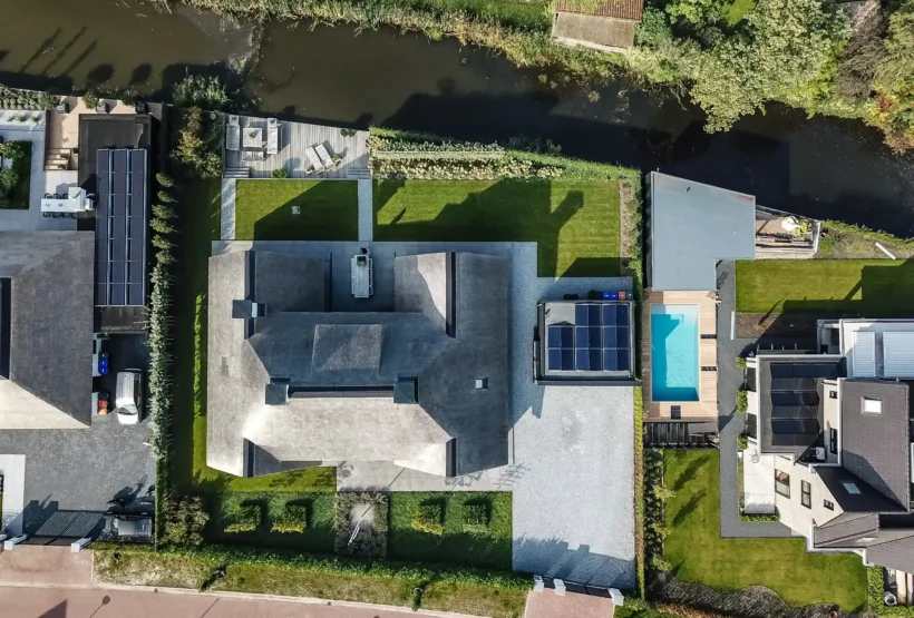 Villa met rieten dak, omringende tuin, grindpaden en water langs het perceel.